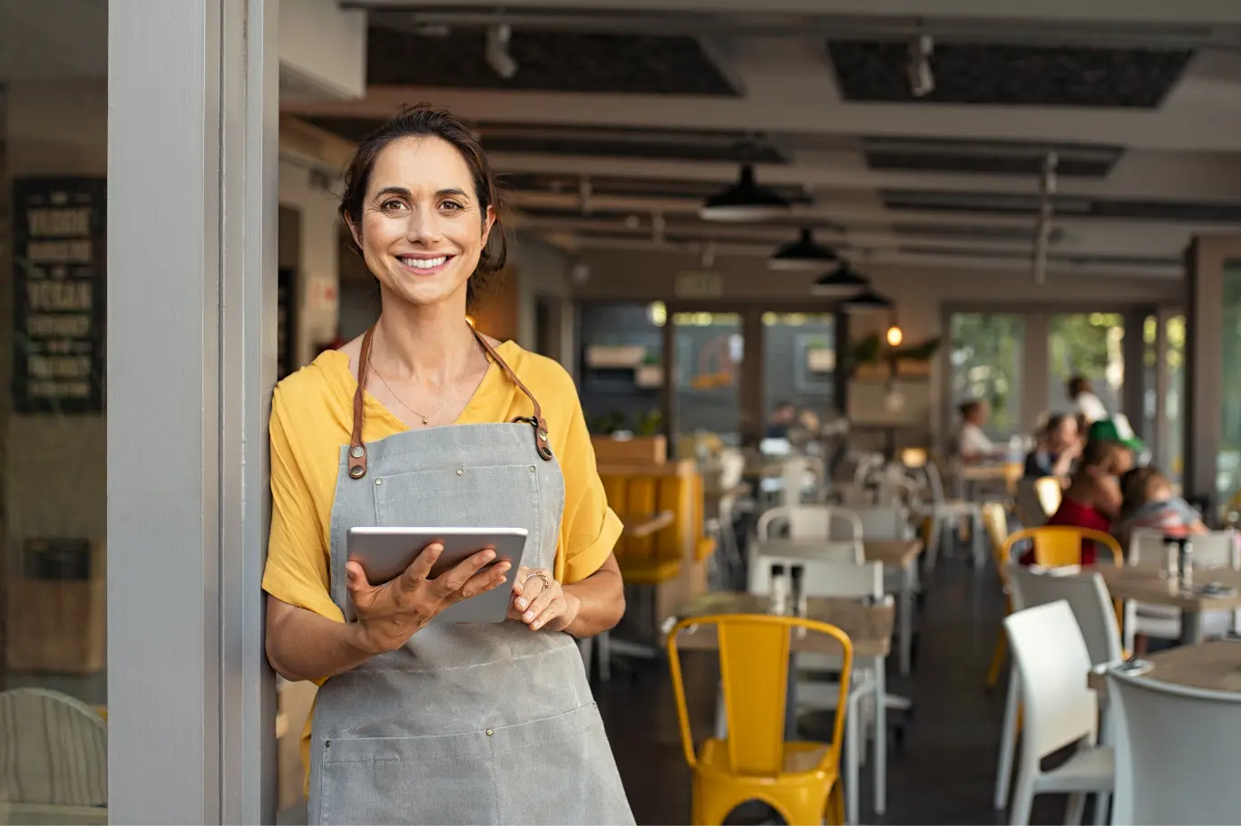 Australian hospitality venue owner using a tablet in her cafe dining room, supported by KSH TAX for POS reconciliation, Hospitality Award payroll and BAS lodgement